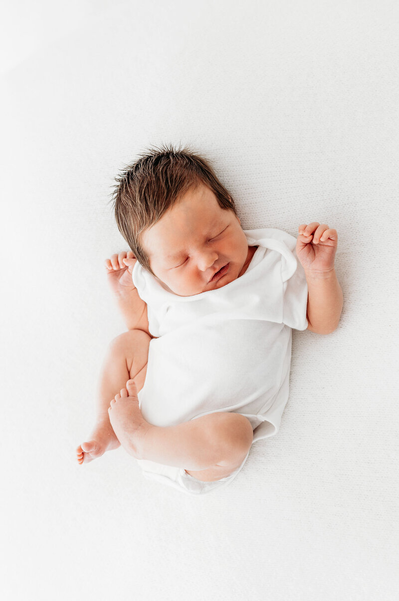 Newborn baby boy laying on white blanket wearing white vest