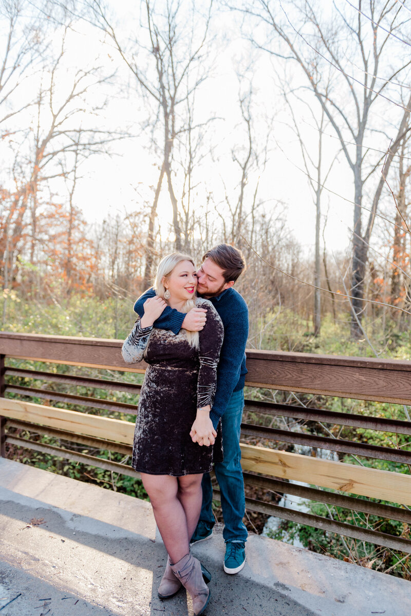 Man wraps arm around woman's should from behind while woman smiles at man.