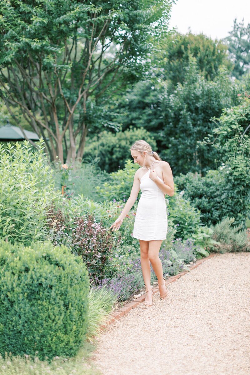 A cute, blonde senior girl walks through a garden scape for her senior photos.