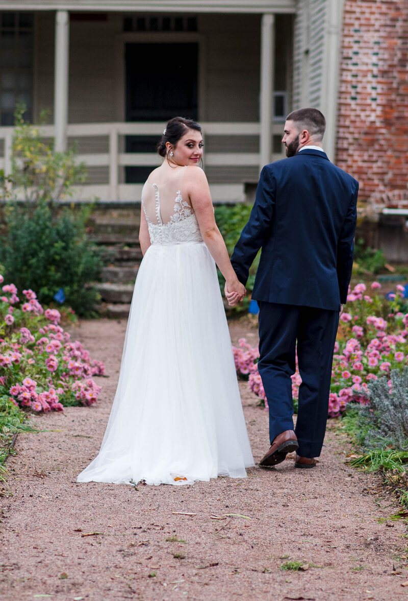 Young caucasian couple walking through a path with grass and roses to a white fenced house.