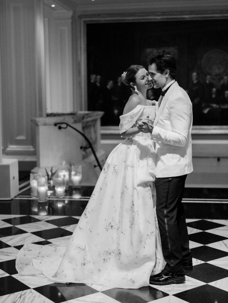 Black and white image of a couple dancing on their wedding day, smiling warmly at each other.