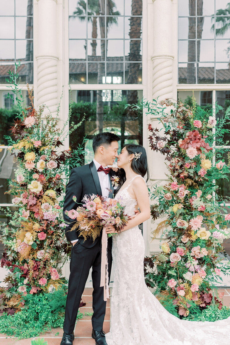 2-alisonbrynn-Radiant-LoveEvents-Maxwell-House-bride-kissing-groom-ceremony-alter-tropical-floral-column-sides-of-couple-outdoors-romantic-elegant-timeless