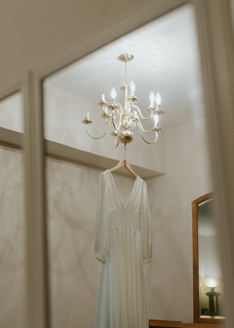 Wedding gown hanging from silver chandelier in tan room