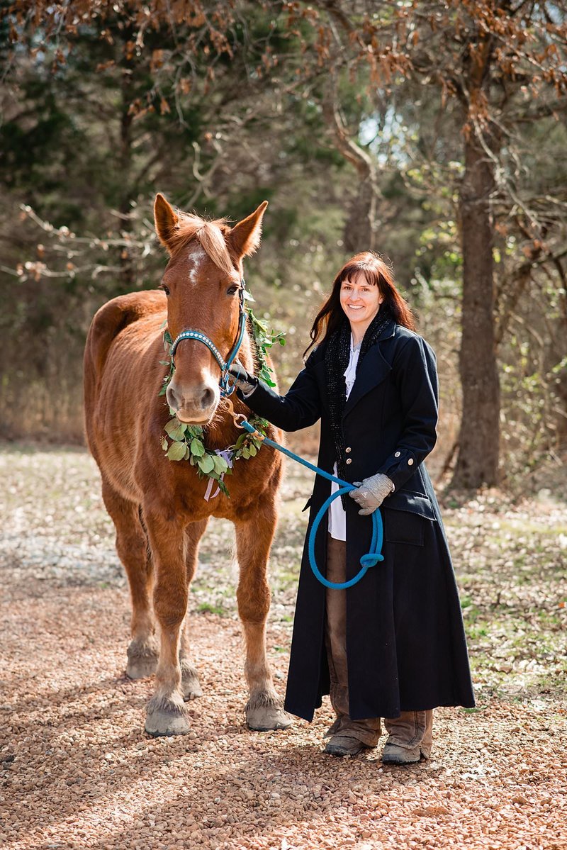 Equestrian owner brand photoshoot wearing long black coat and holding lead for her horse