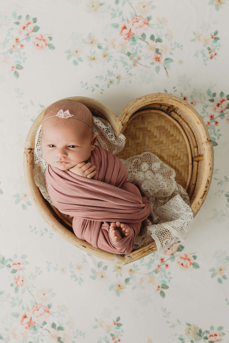 newborn baby girl wrapped in a soft peach wrap with her toes poking out and a tiny pink bow on a newborn bed during newborn session in harrisburg pa