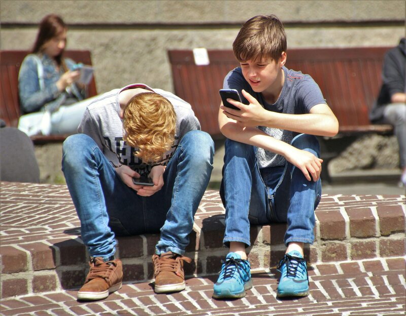 2 teen boys on phones outside on brick wall