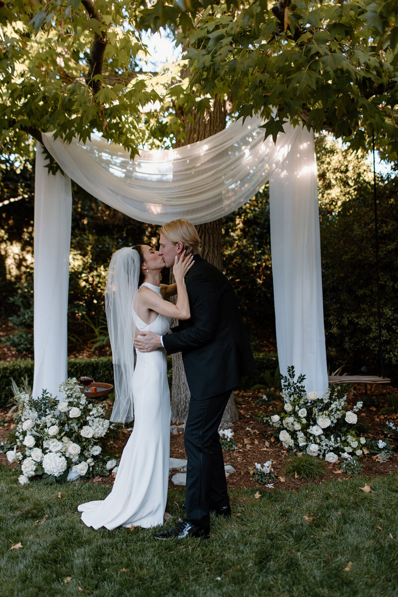 6-radiant-love-event-2021-outdoor-ceremony-bride-groom-kissing-white-flowy-draping-tree-backdrop-romantic-elegant-timeless