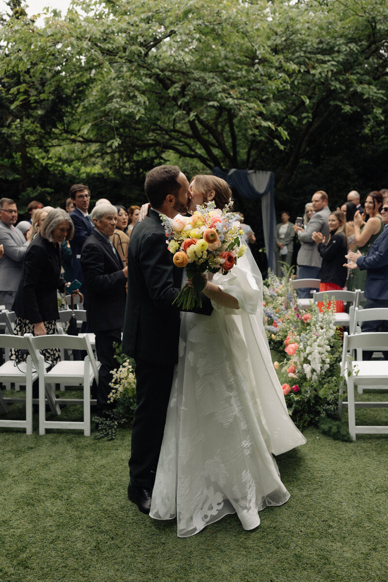 Couple walking hand in hand sharing a kiss during their wedding day, captured in an artistic photojournalistic style with digital and film photography
