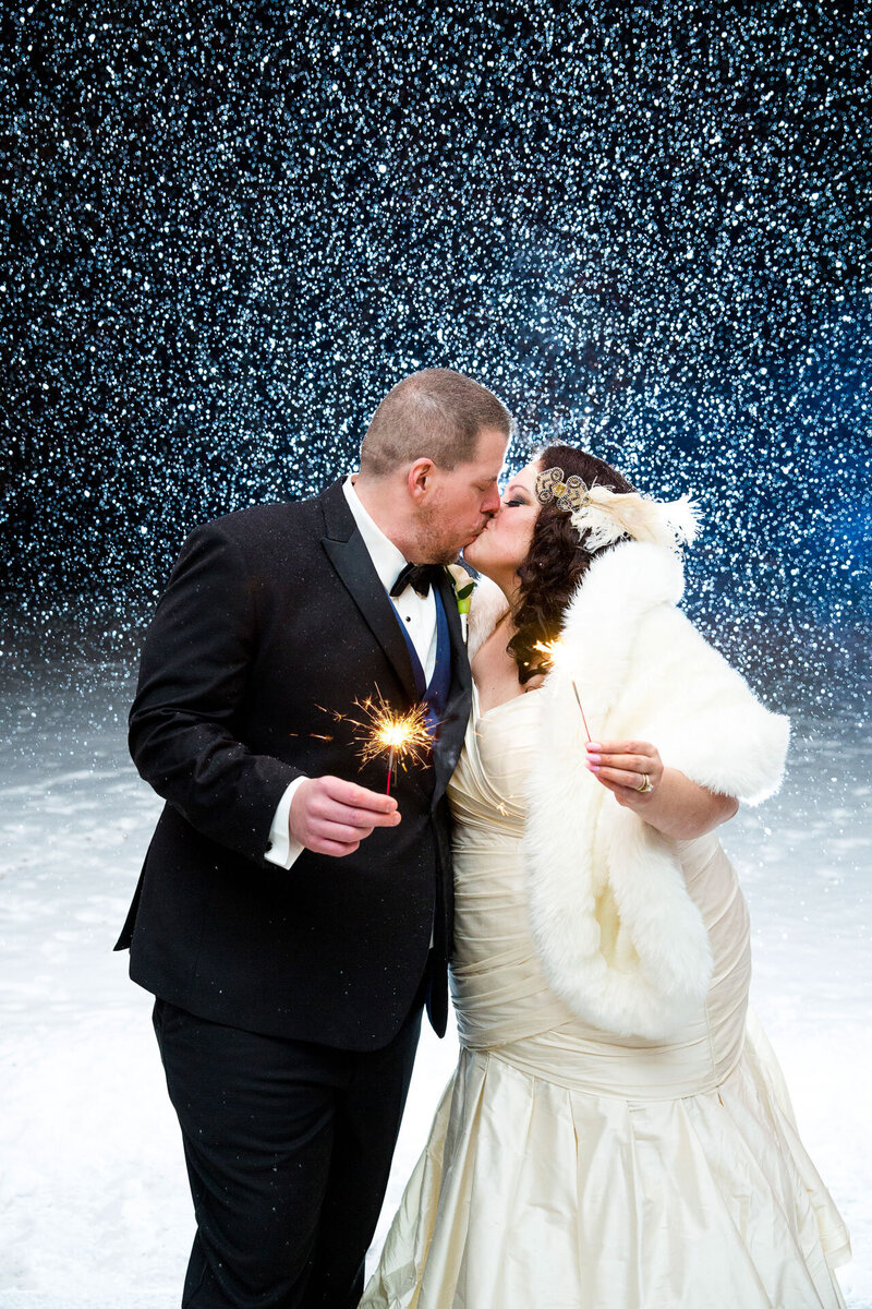 Bride and groom holding sparklers with snow in background