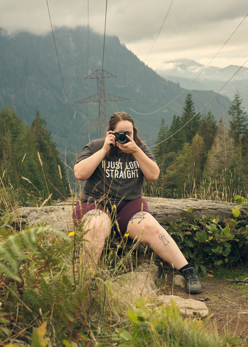 Allison Haley Photography sits on a rock on a hiking trail with her camera