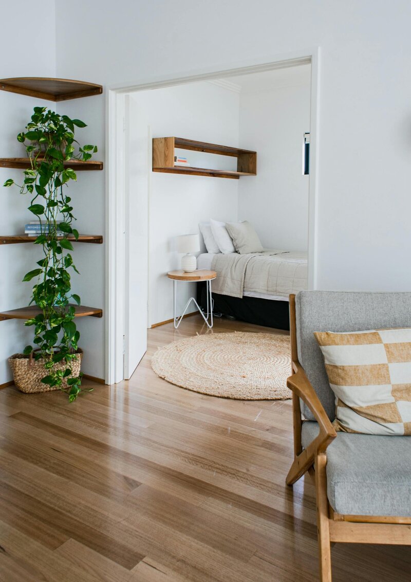 Clean house with green drapnig plaint, natural fabric rug and bed linen, chair in forground