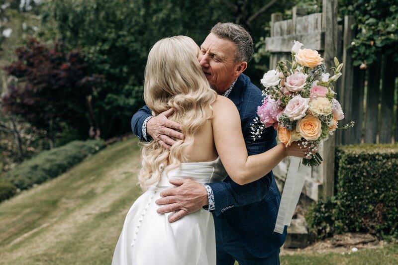 candid wedding photo of bride hugging father with pastel bouquet near southland
