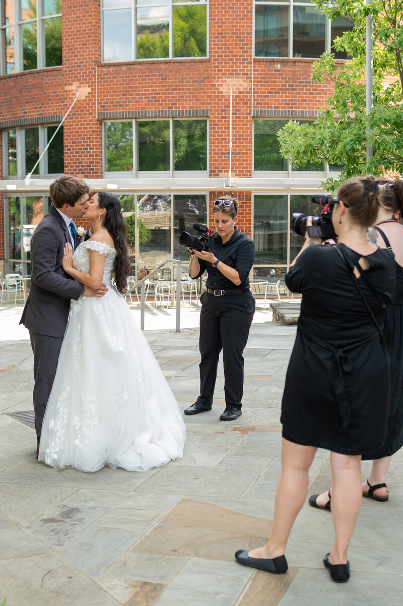 A newlywed couple kissing and being photographed 