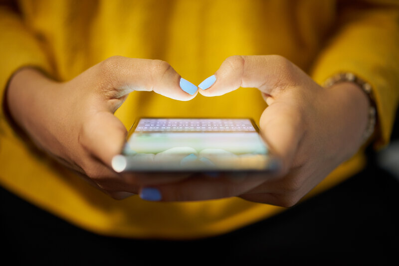 Woman in a yellow sweatshirt scrolling social media on her mobile phone