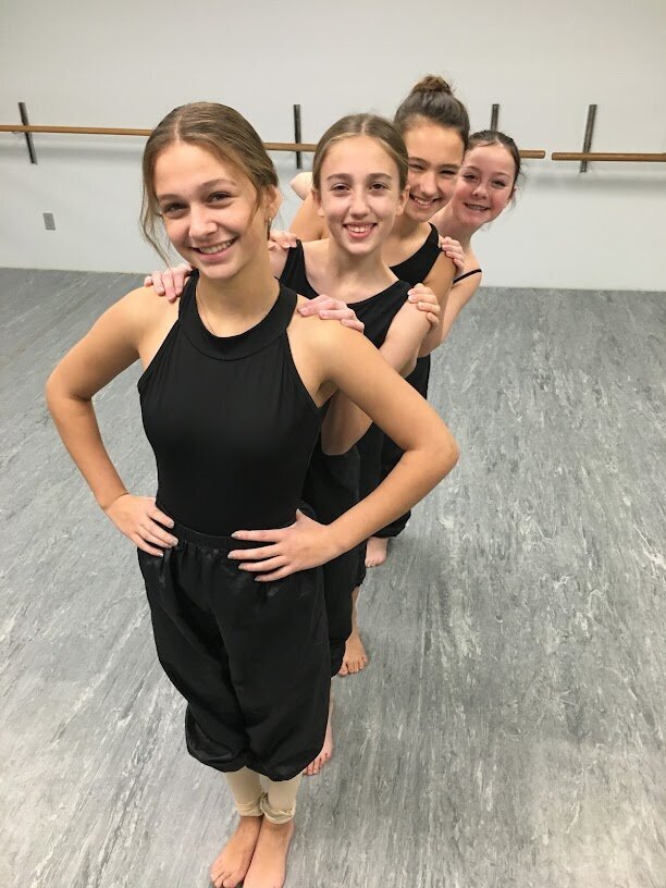 four teen dancers standing in a line looking over each others shoulders smiling