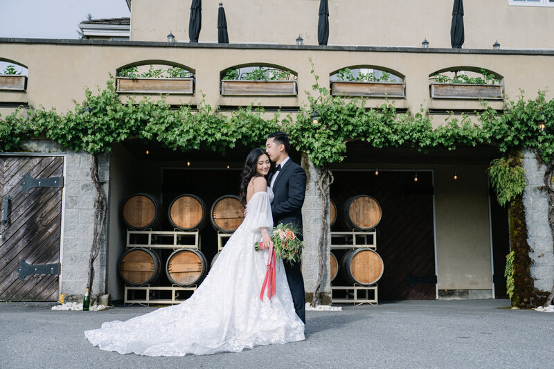 Woodinville vineyard estate wedding portraits in front of wine barrels white lace dress and floral bouquet