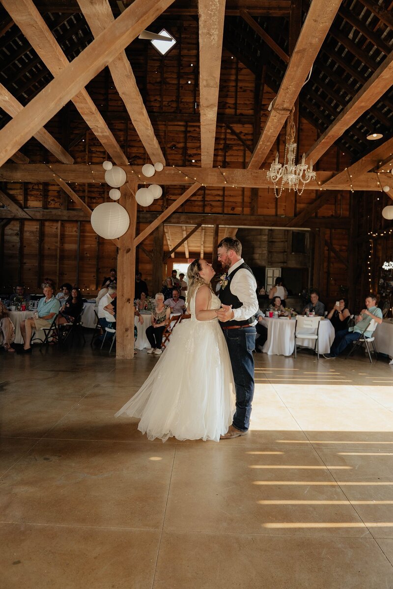 Bride and groom dancing together inside a barn reception