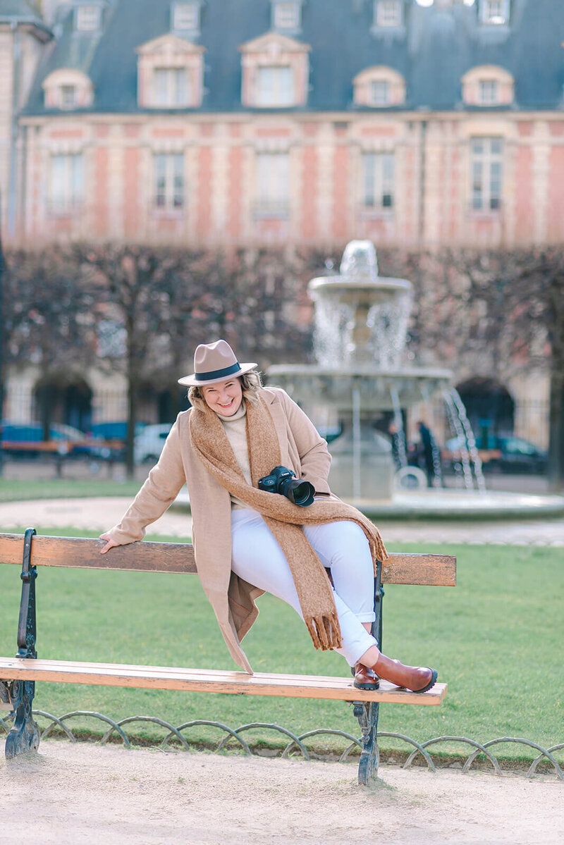Rachael Laporte, Paris Photographer, sitting on bench laughing with camera in hand