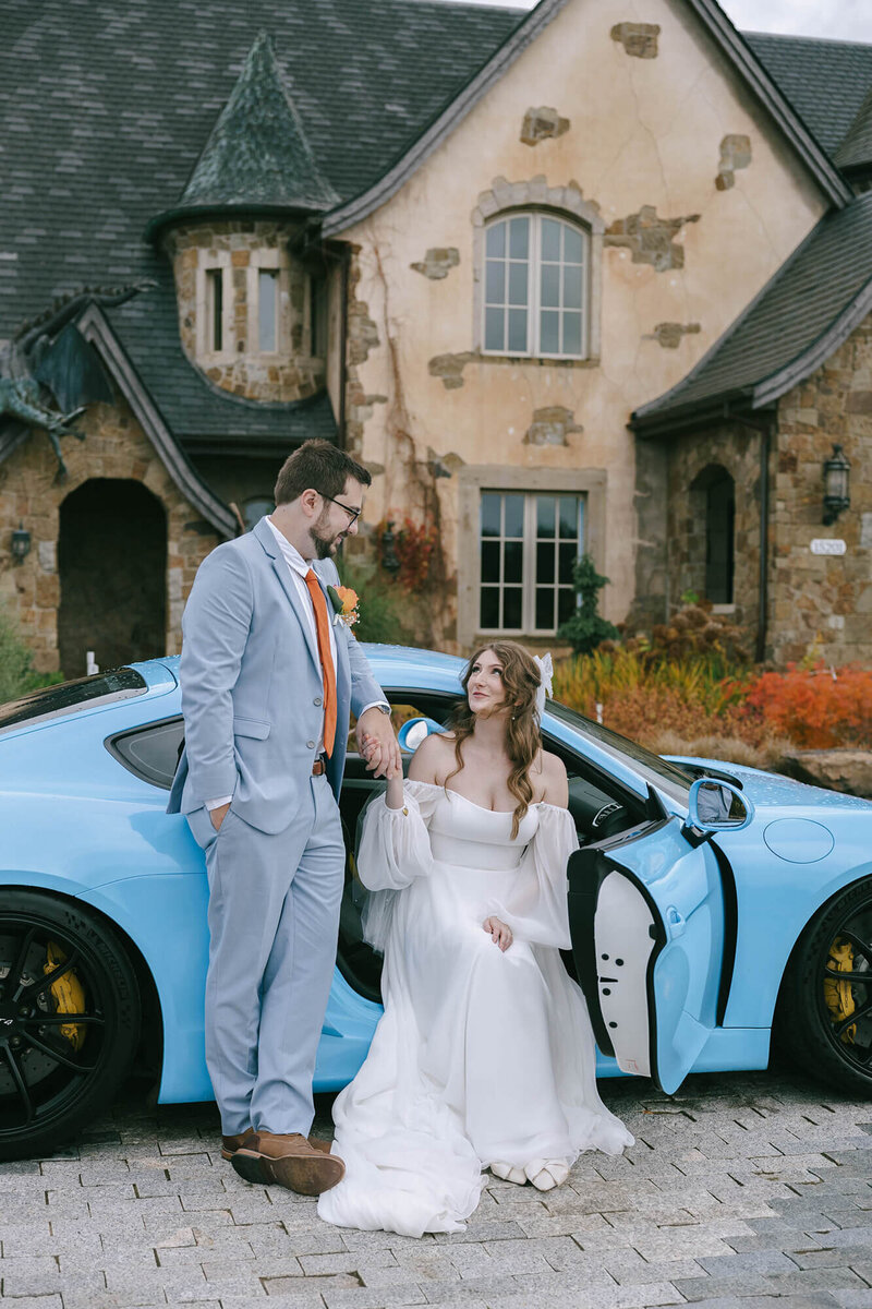 A bride and groom with a blue car in front of a castle, representing an event planned by Eugene wedding planners Birdie June Events & Rentals. 