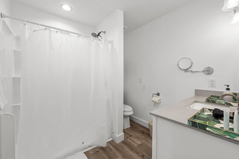 Simple, spacious bathroom with bright white shower curtain and tropical-themed trays, perfect for vacationers in PCB or 30A rentals.