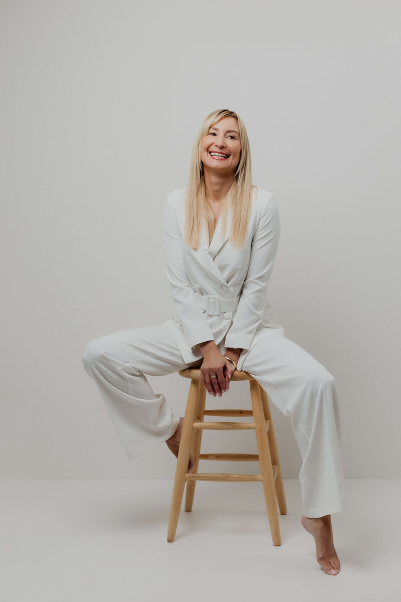 A women laughing in a white suite sitting on a chair.