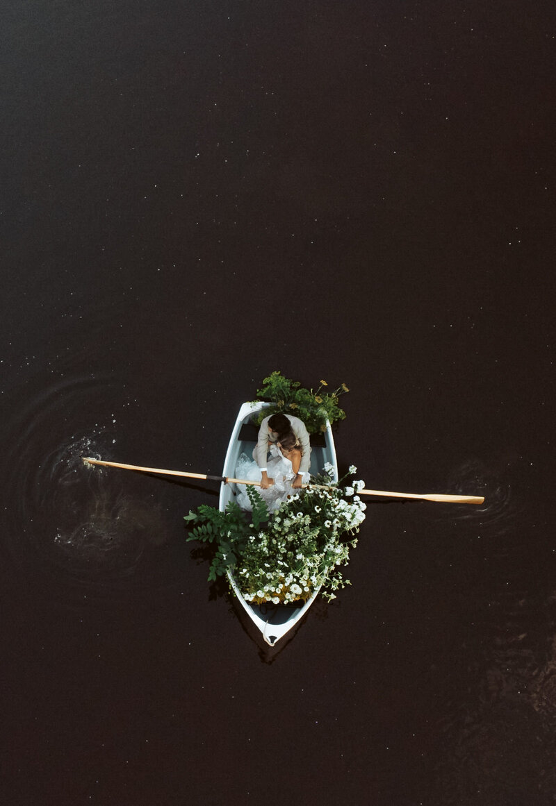 Bride and groom in a flower-decorated rowboat during their Maine elopement, photographed from above on the water.