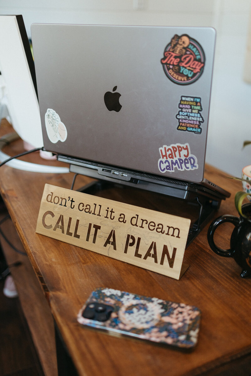 SEO strategist laptop on a wooden desk with an inspirational sign and cellphone sitting in front of it.