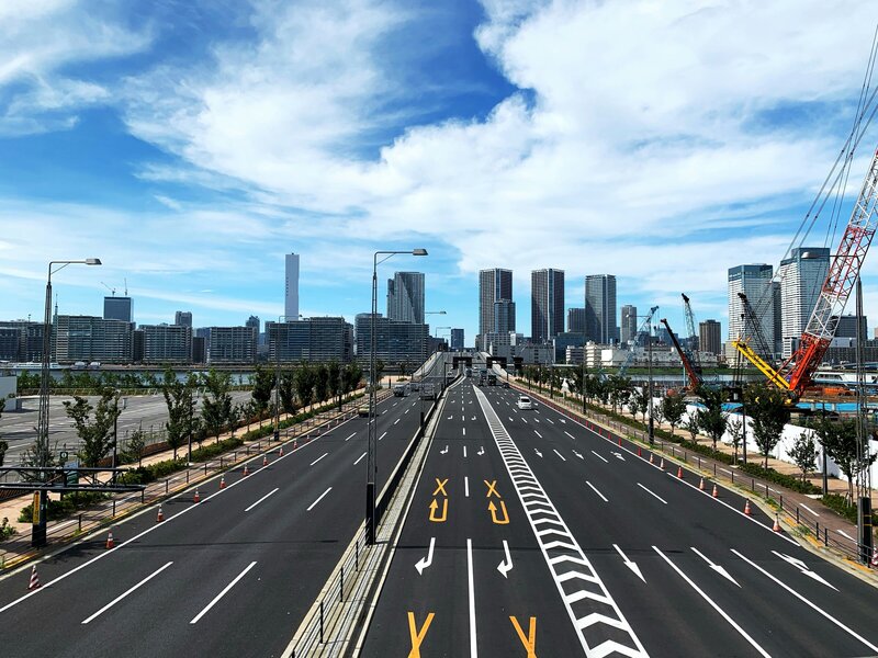 Wide-angle shot of a modern expressway leading into Tokyo’s skyline, under a bright blue sky with light clouds, capturing the spirit of smooth drives and city exploration.