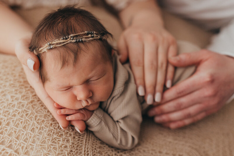 Family session photo of newborn baby being cradled by tattooed arms