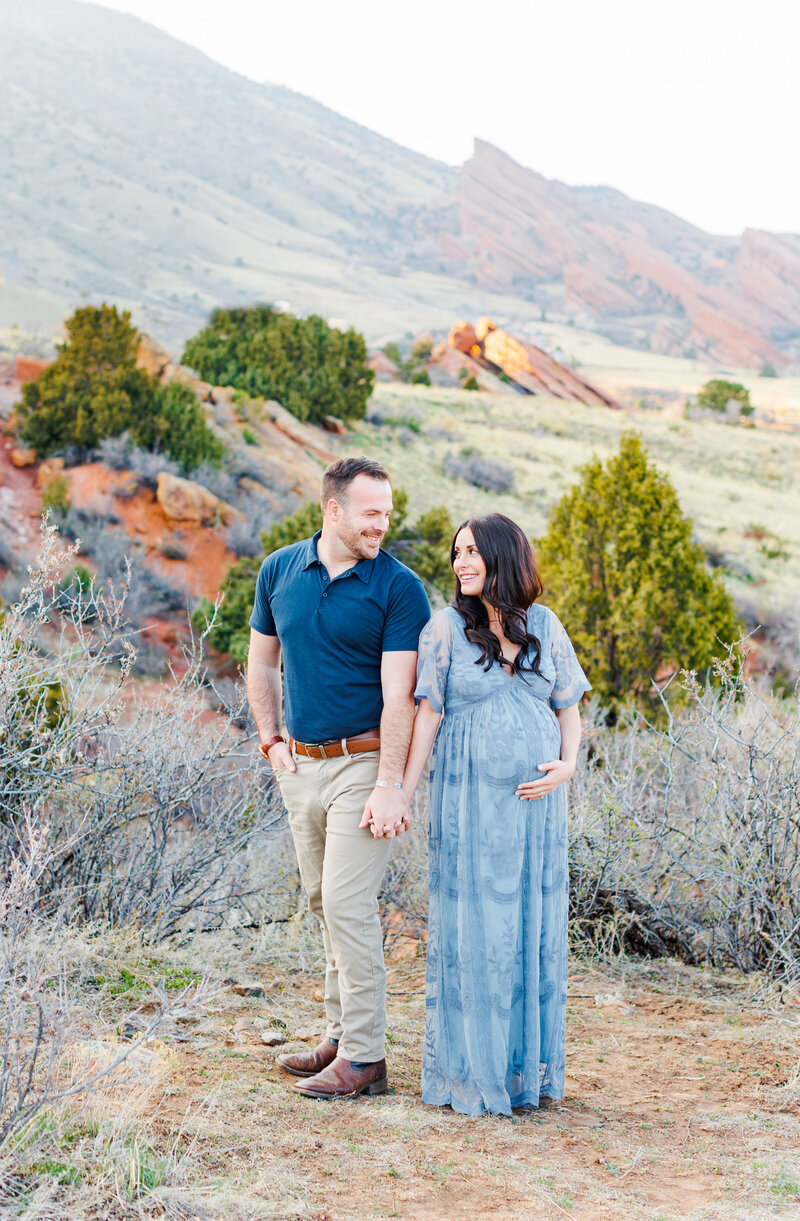 expecting mom and dad snuggle close together on mountain with volcanic rock in st. george utah for maternity photos