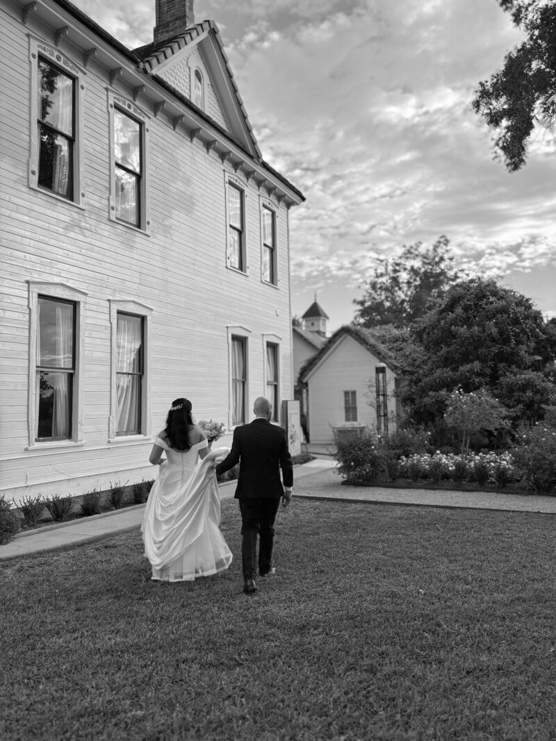 Black and white photo of a bride and groom walking toward a building