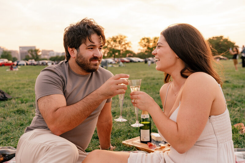 A couple cheers with champagne in a park