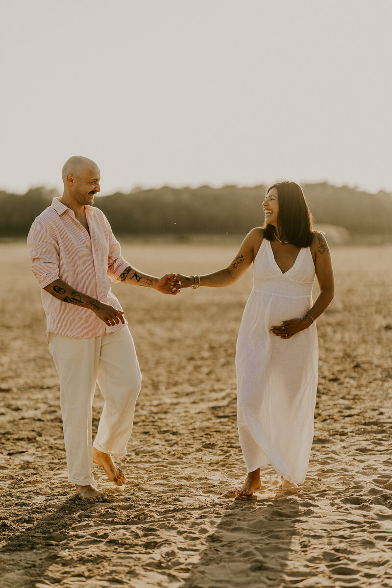 Femme enceinte de profil, robe en dentelle blanche, tournant le dos à l'océan, capturée par Laura, photographe en Vendée lors d'un shooting photo.