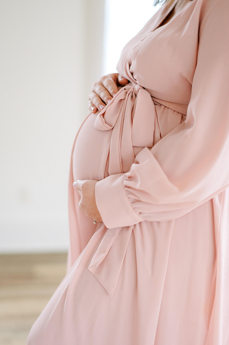 Pregnant woman in a pink dress poses with her hands on her bump