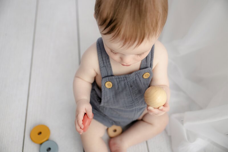 7 month little boy sitting playing wooden toys dressed in a blue romper