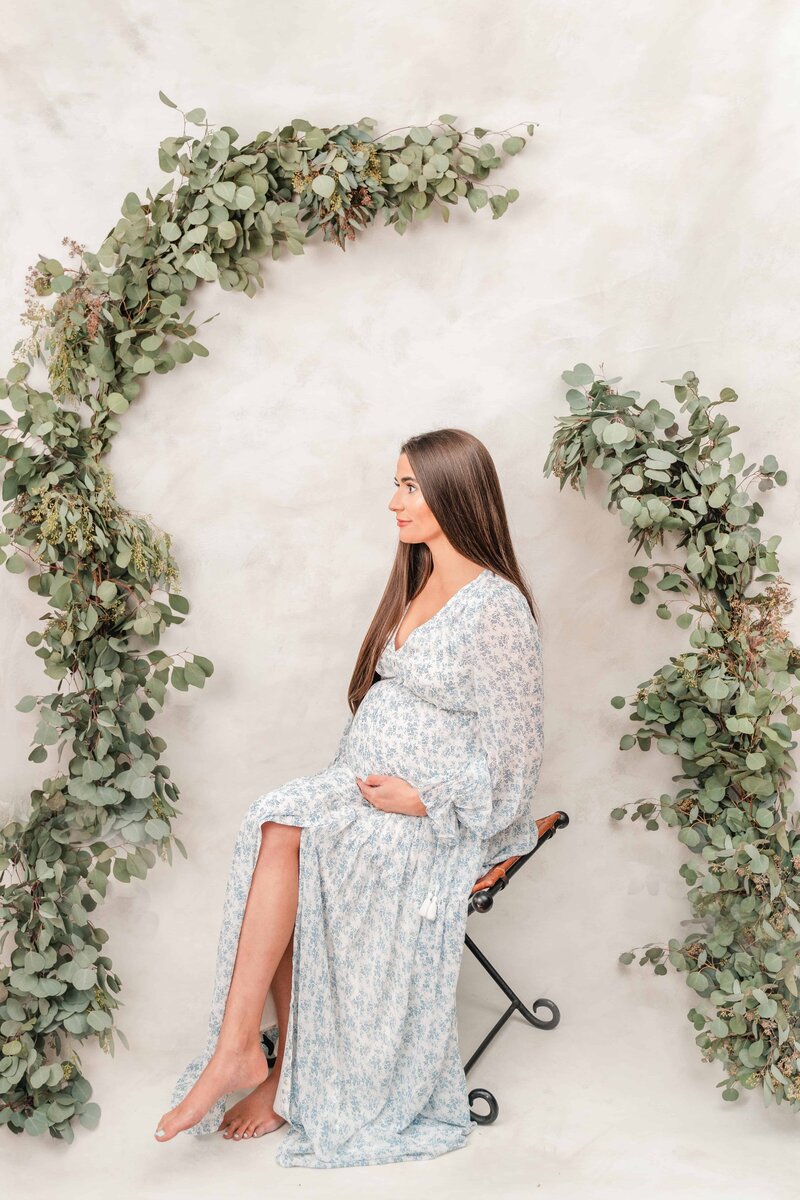 Expecting mother sits in front of style backdrop.