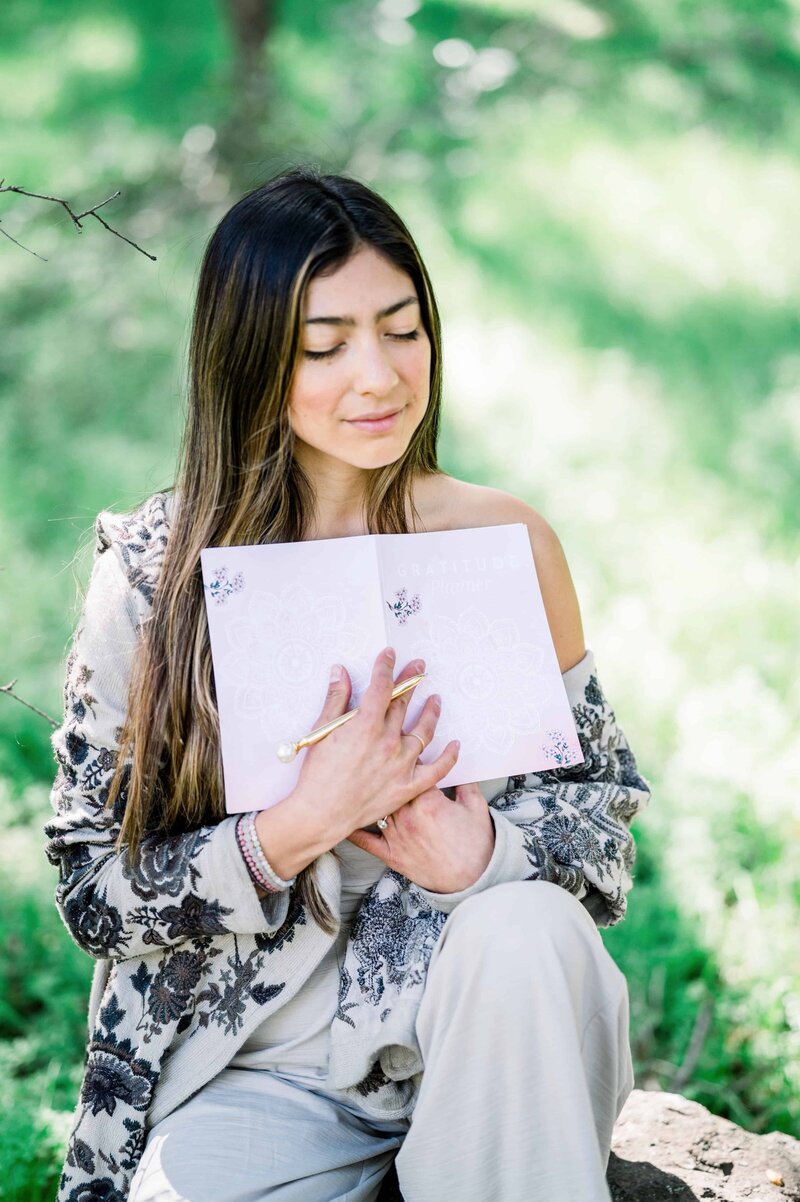 Woman sits in reflection holding a journal next to her heart