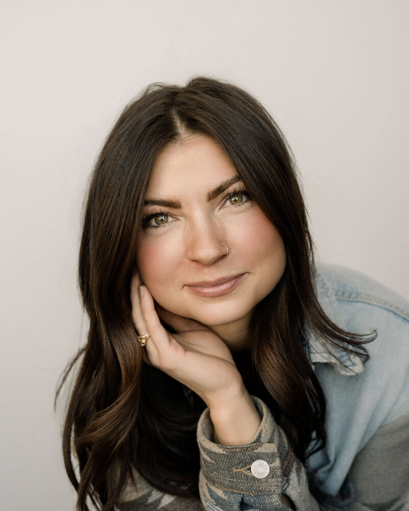 A Parker photographer looks down at her camera while smiling in her studio, she is wearing a denim jacket with an aztec neutral designed sleeve.