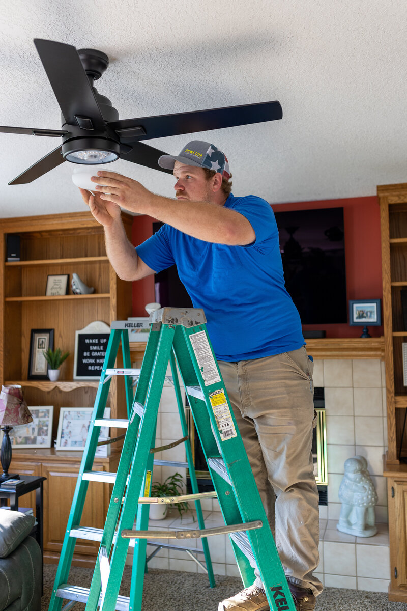 Licensed residential electrician in Iowa installing ceiling fan and light fixtures during home electrical repair and lighting service.