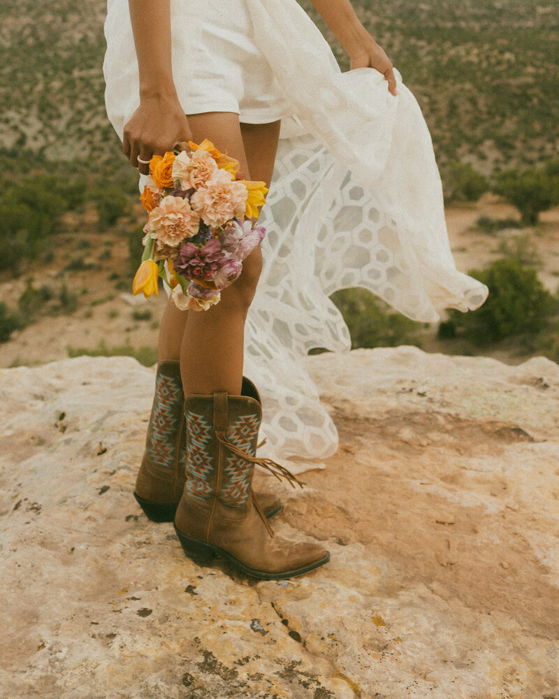 girl wearing white dress, cowboy boots holding bouquet of flowers