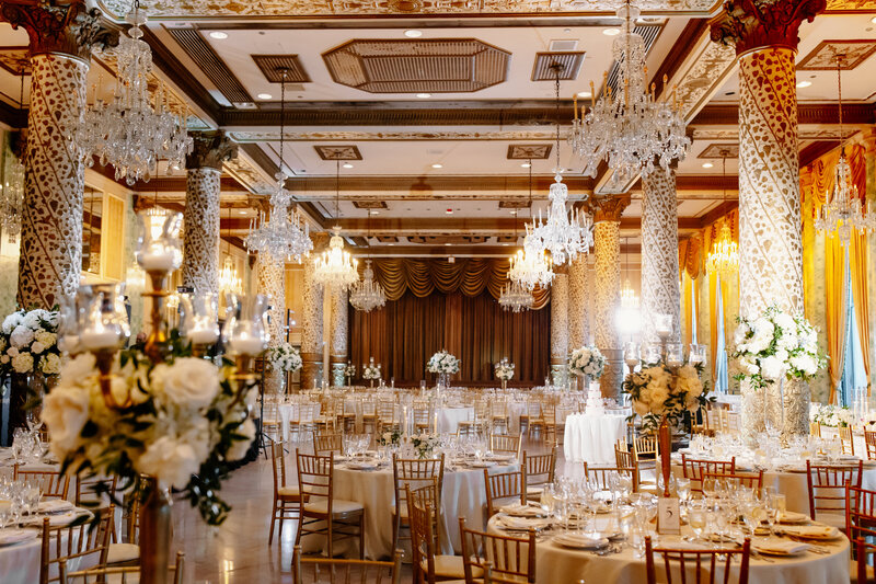 Upscale ballroom wedding reception with chandeliers, round tables and large floral decorations with white roses.