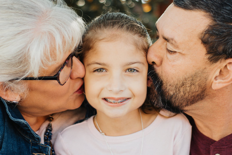girl being kissed on each cheek by parents