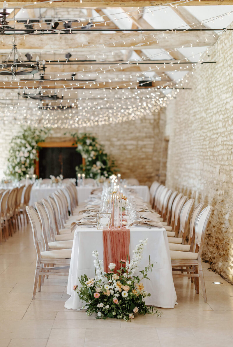 Long banquet-style table in the barn at Caswell House with florals and fairy lights above