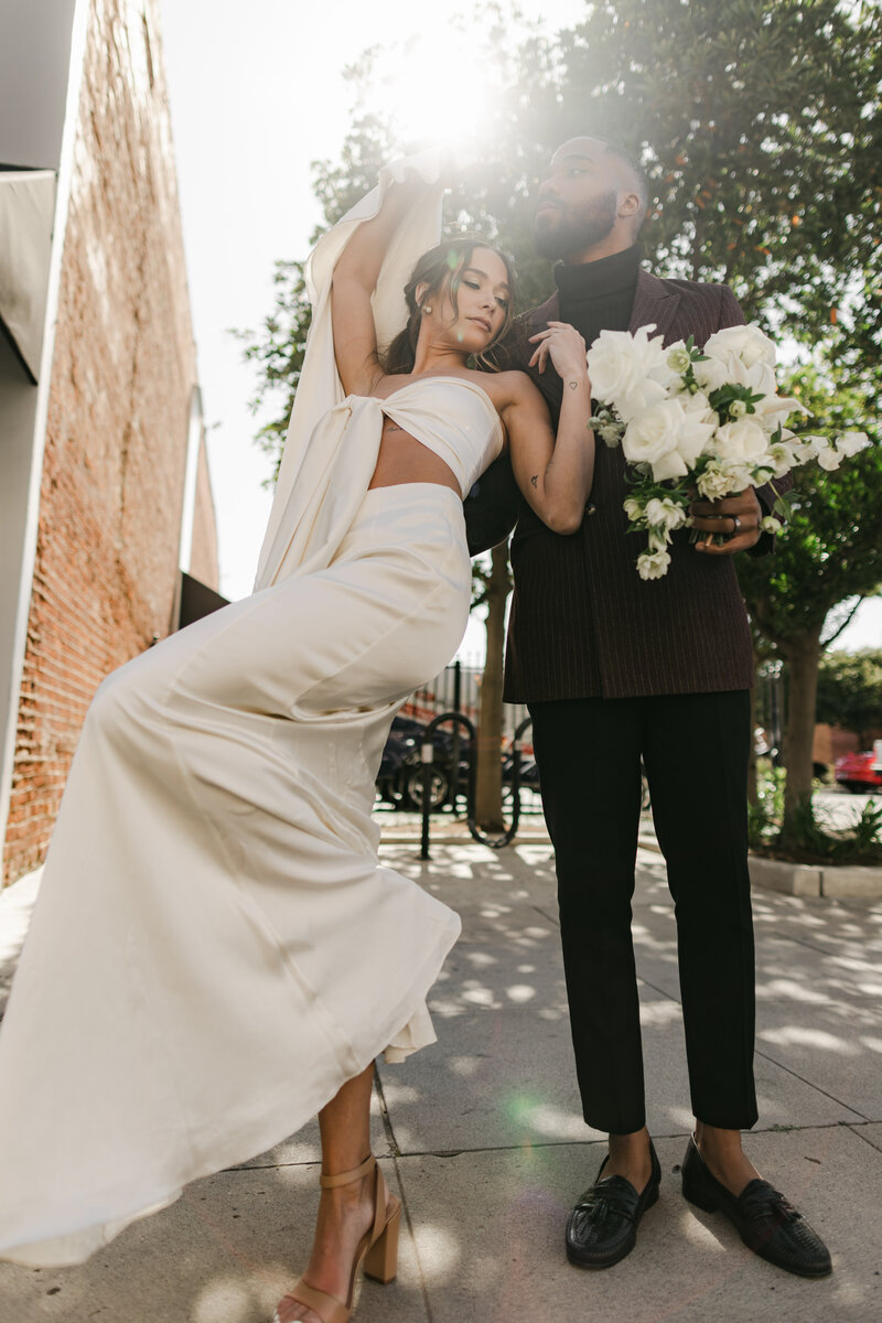 Fashion-forward editorial wedding portrait of a stylish couple in modern attire, with dramatic movement and bold light in a Fresno CA city setting.