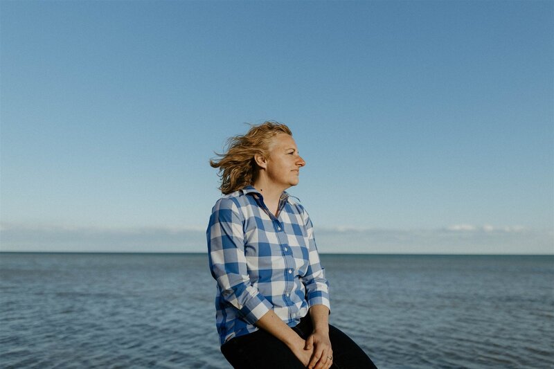 Writer, Sarah Freymuth, leans against a tree and looks off into the distance in a blue t-shirt