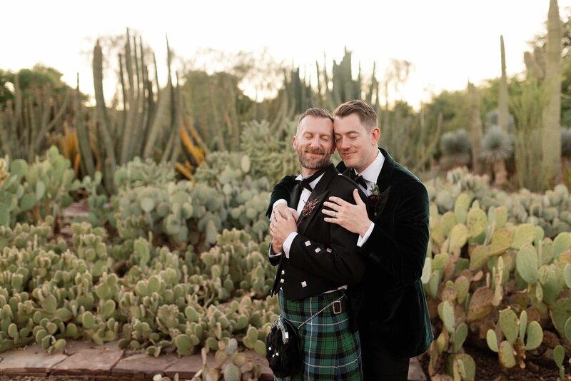 Two grooms cuddle and close eyes together in cactus garden.