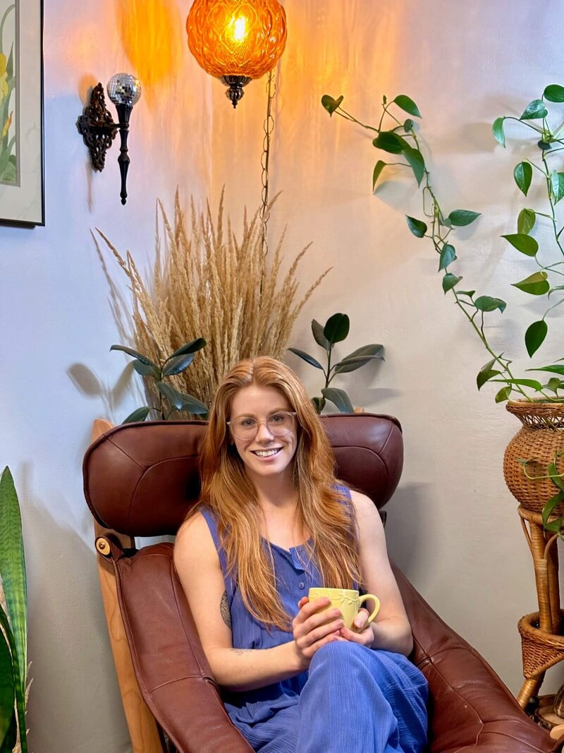 Eugene licensed professional counselor, Emily sits in a chair with a cup of tea.,