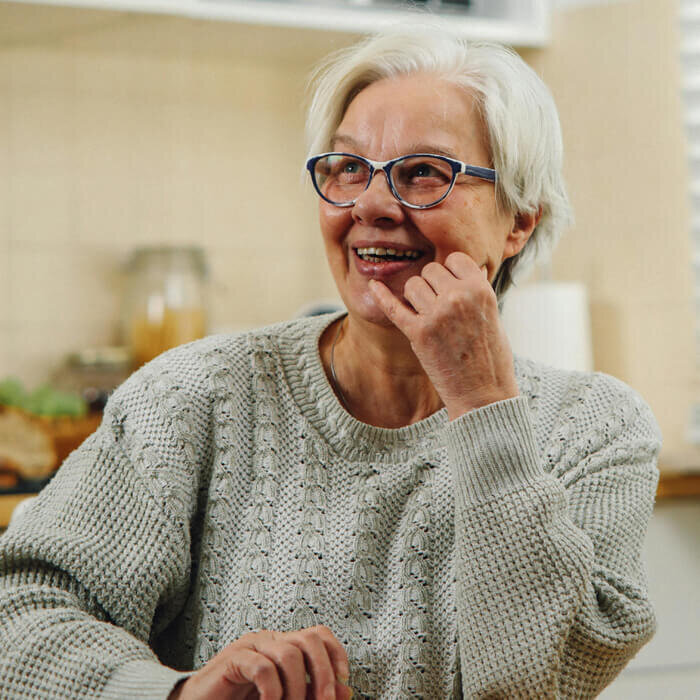 A senior woman in a sweater sitting at her kitchen table