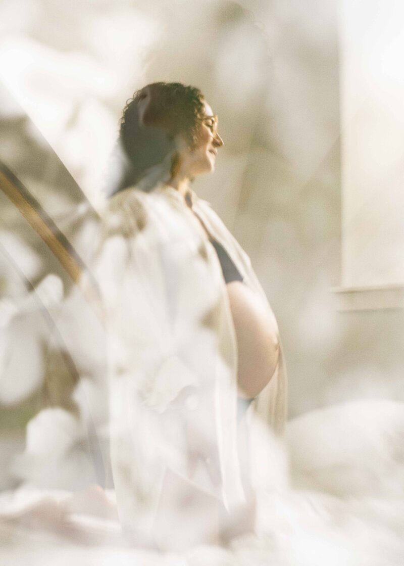 Expecting pregnant woman is kneeling on the bed with bare belly in full view.