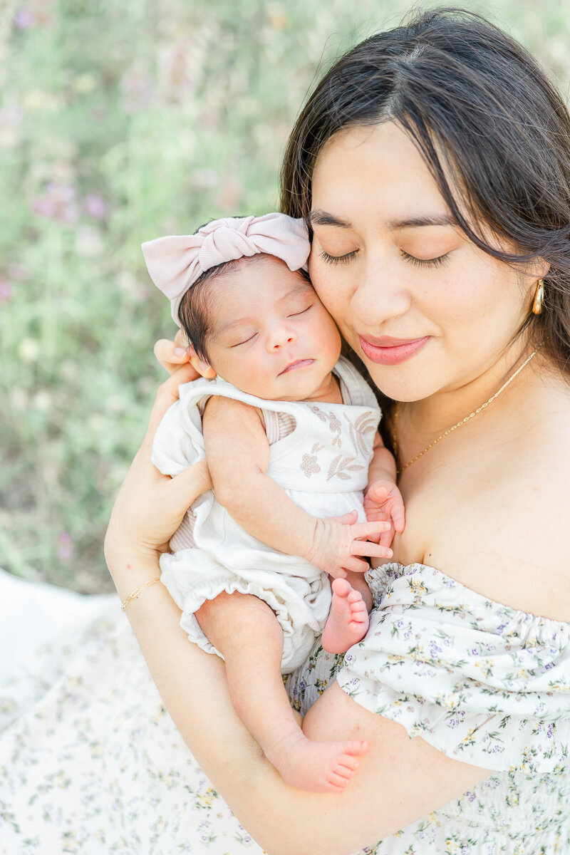 a mom holds her newborn girl up to her cheek and closes her eyes.
